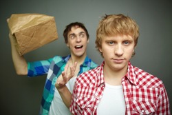 Crazily looking guy exploding paper bag behind his friend's back, fool's day series or birthday party