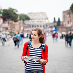 Pretty young female tourist holding a map while walking along the Via del Fori Imperiali avenue in Rome, Italy (with Colosseum in the background)