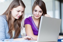 Two female college students working on a laptop computer during class (color toned image)