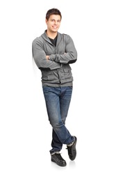 Full length portrait of a happy young man leaning against wall isolated on white background
