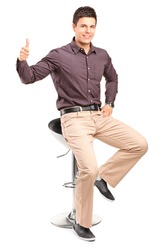 A young man sitting on high chair and giving thumb up isolated on white background