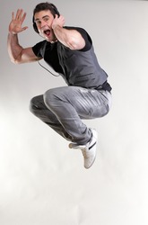Young man jumping and listening music isolated over a gray background