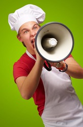 portrait of a young cook man screaming with a megaphone over a green background