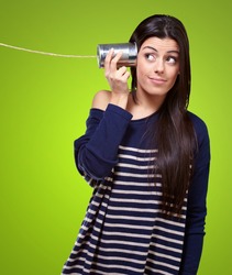 portrait of a young woman hearing through a tin can over a green background