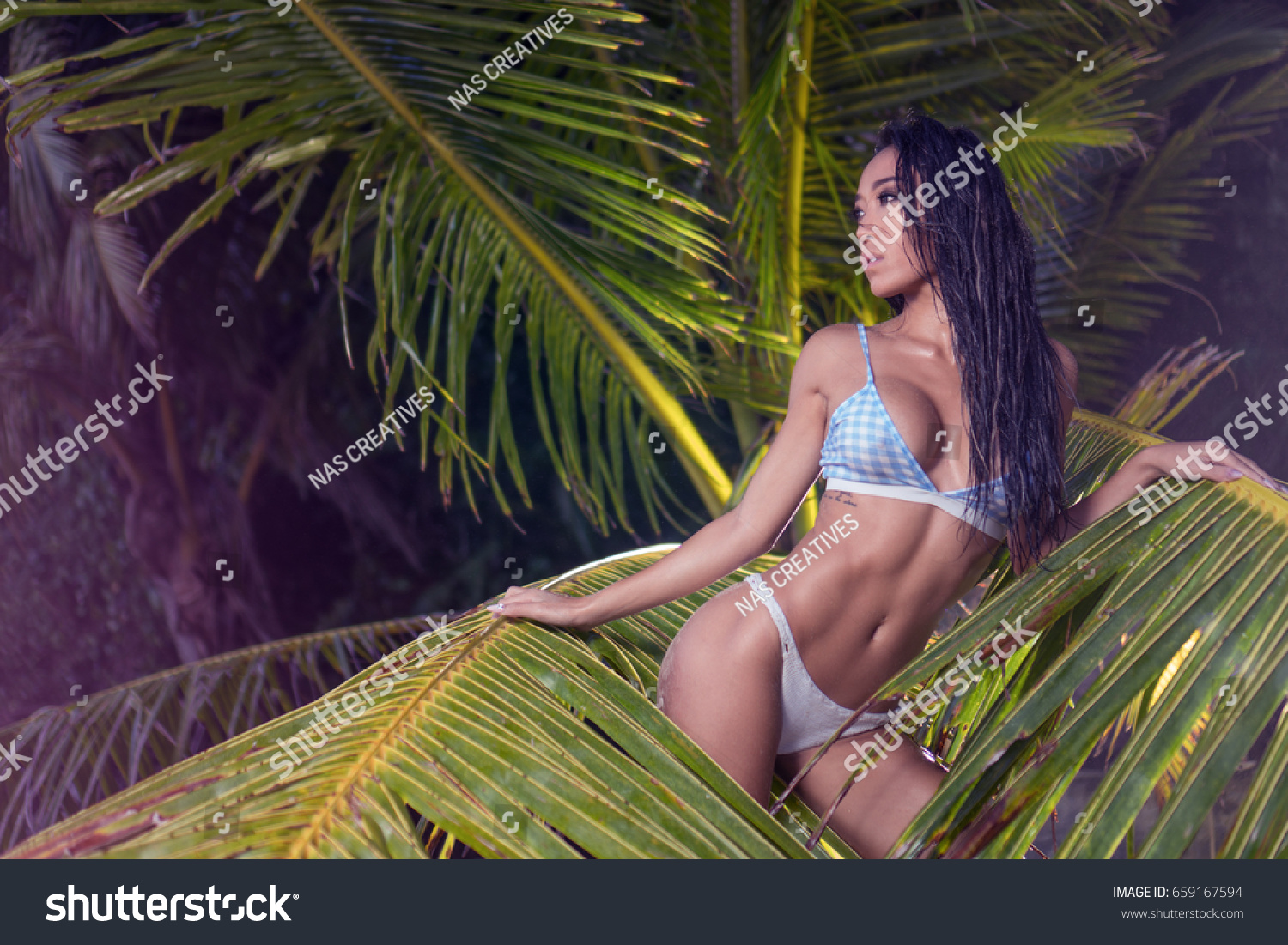 Молодая брюнетка стягивает красный бикини и позирует под пальмой