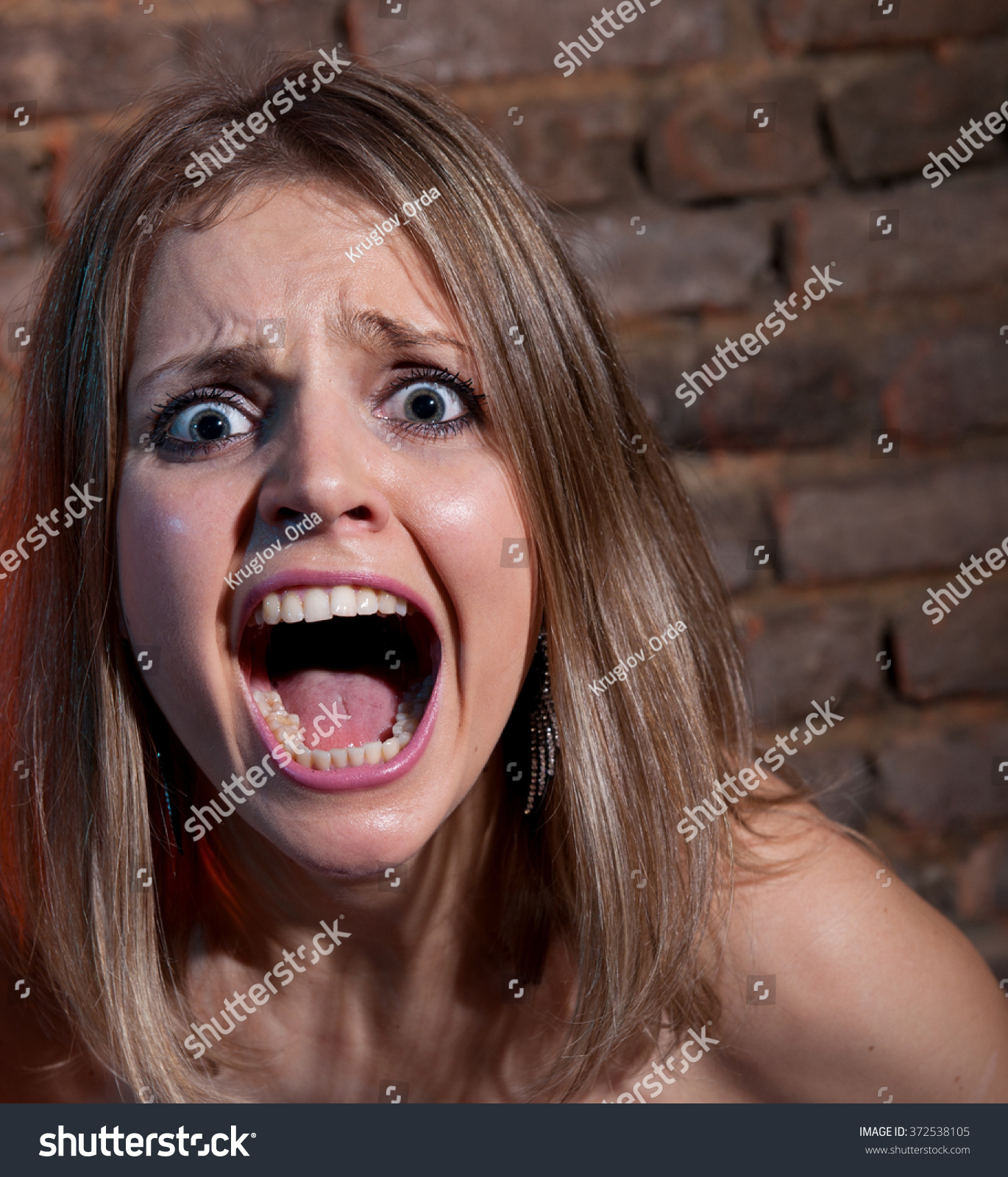 Woman Screaming In Terror On The Brick Wall Background Stock Photo