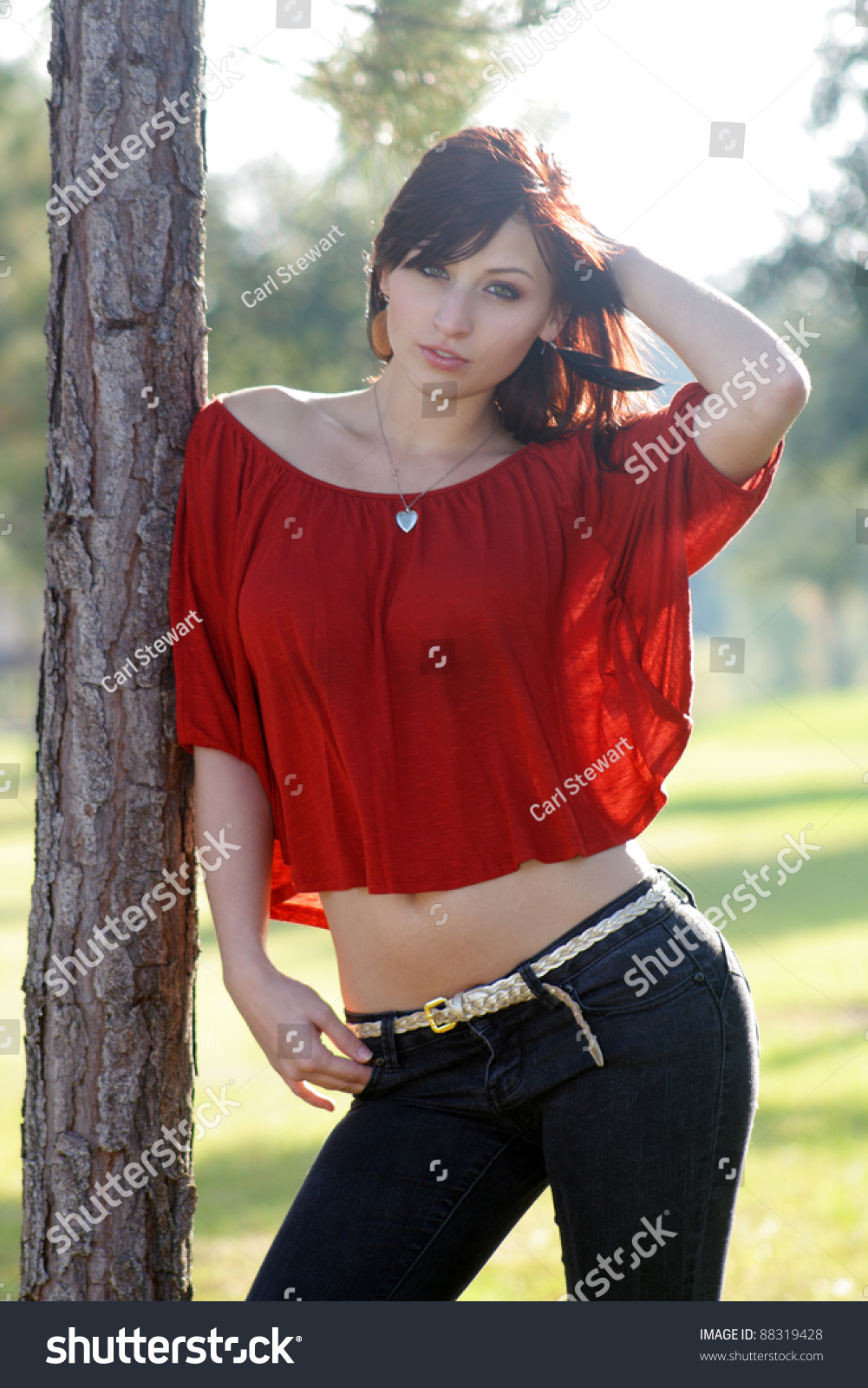 A Beautiful Young Woman With Auburn Hair Leans Against A Tree Backlit 