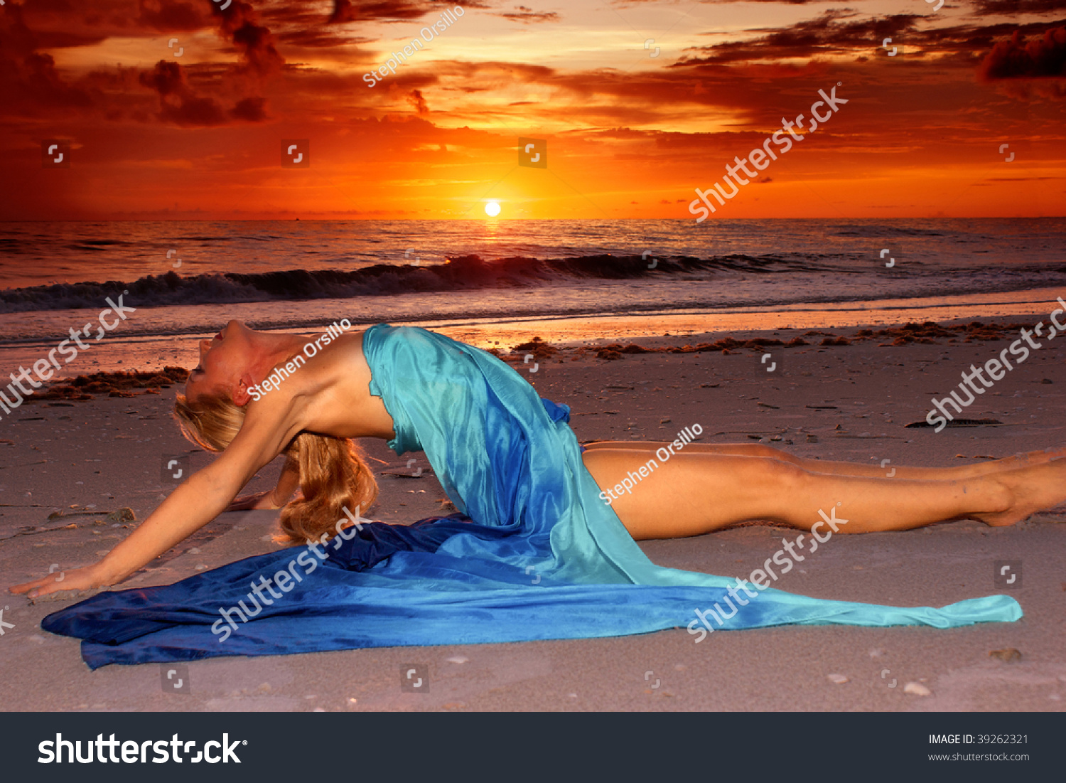 A Long Haired Blonde Woman Is Stretched Out On The Beach At Sunset In