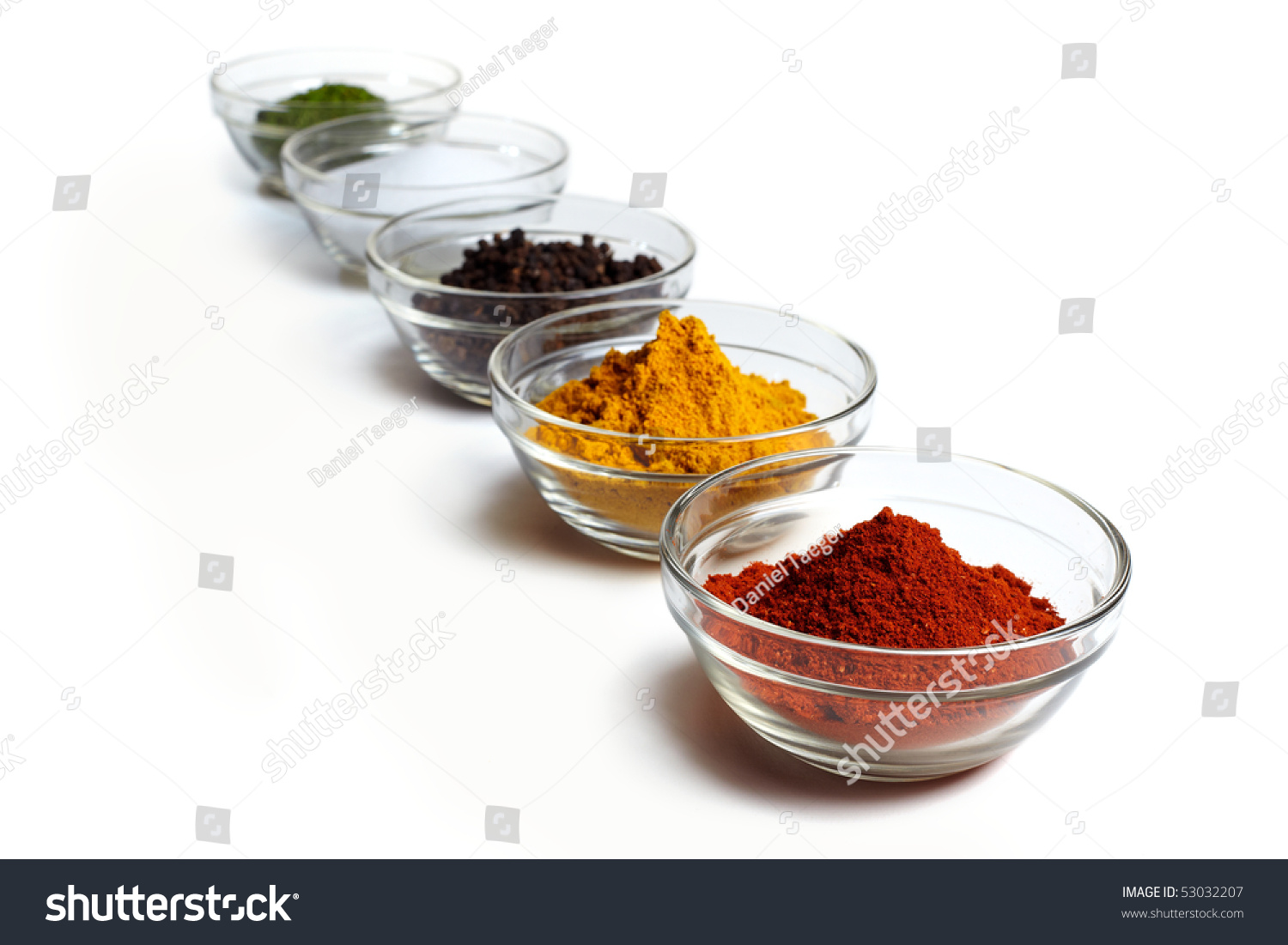 Assortment Of Coloured Spices In Glass Bowls In A Row Over White