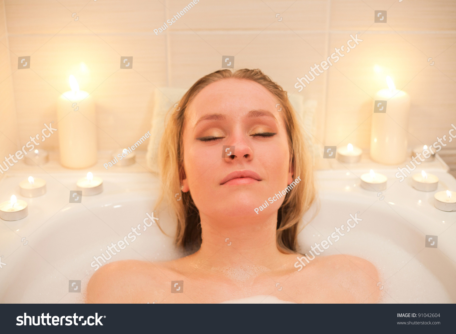 Attractive Young Blond Woman Lying In Bubble Bath With Candles
