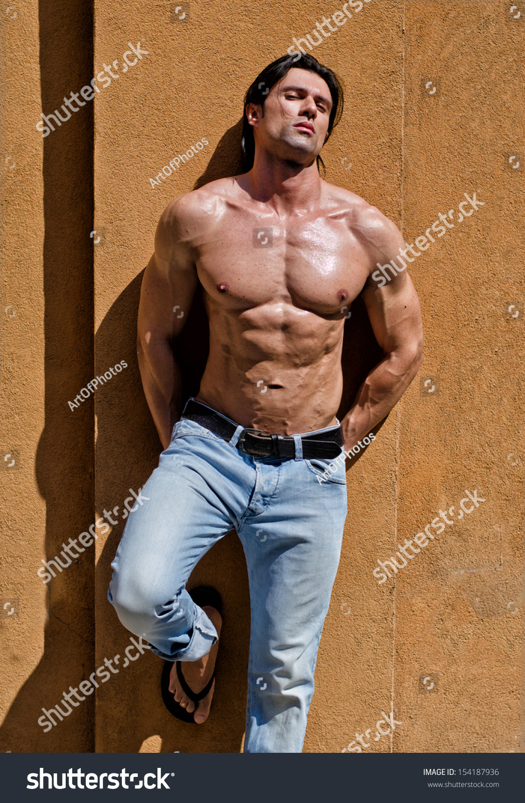 Attractive Young Man Shirtless With Jeans Leaning Against A Wall With