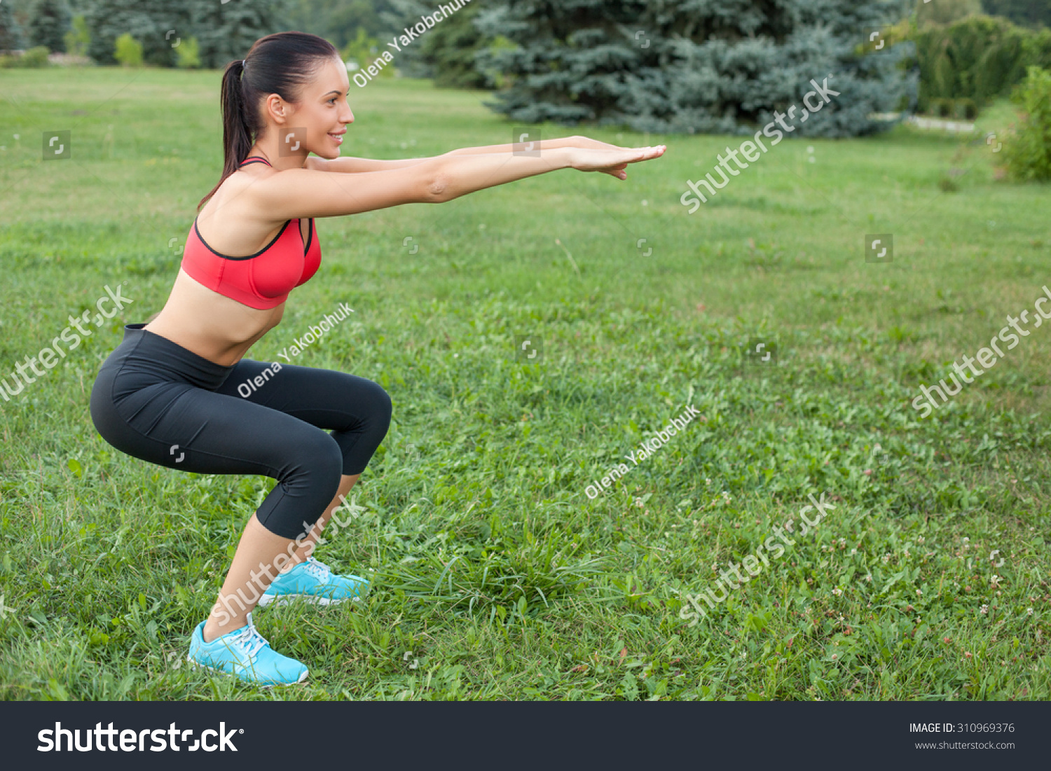Beautiful woman is doing squats in park She is stretching her arms forward The sportswoman is smiling happily Copy space in right side Beautiful woman is doing squats in park She is stretching her arms forward The sportswoman is smiling happily Copy space in right side