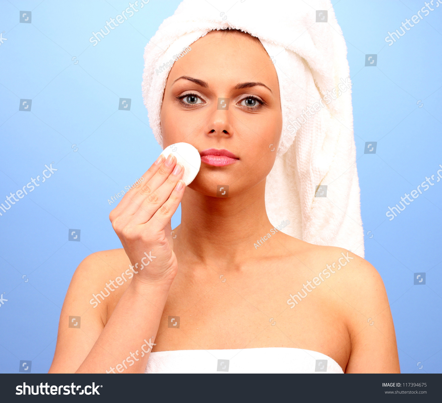 Beautiful Young Woman After Shower With A Towel On Her Head And A Cotton Pad In Hand On Blue 