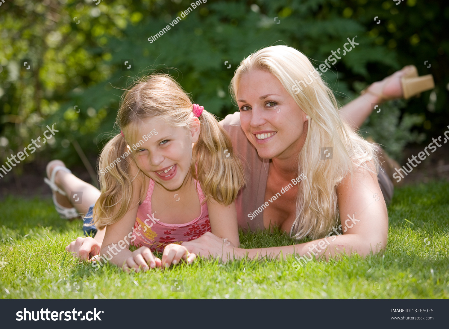 Blond Mother With Her Daughter Lying In The Grass On A Summer Day Stock