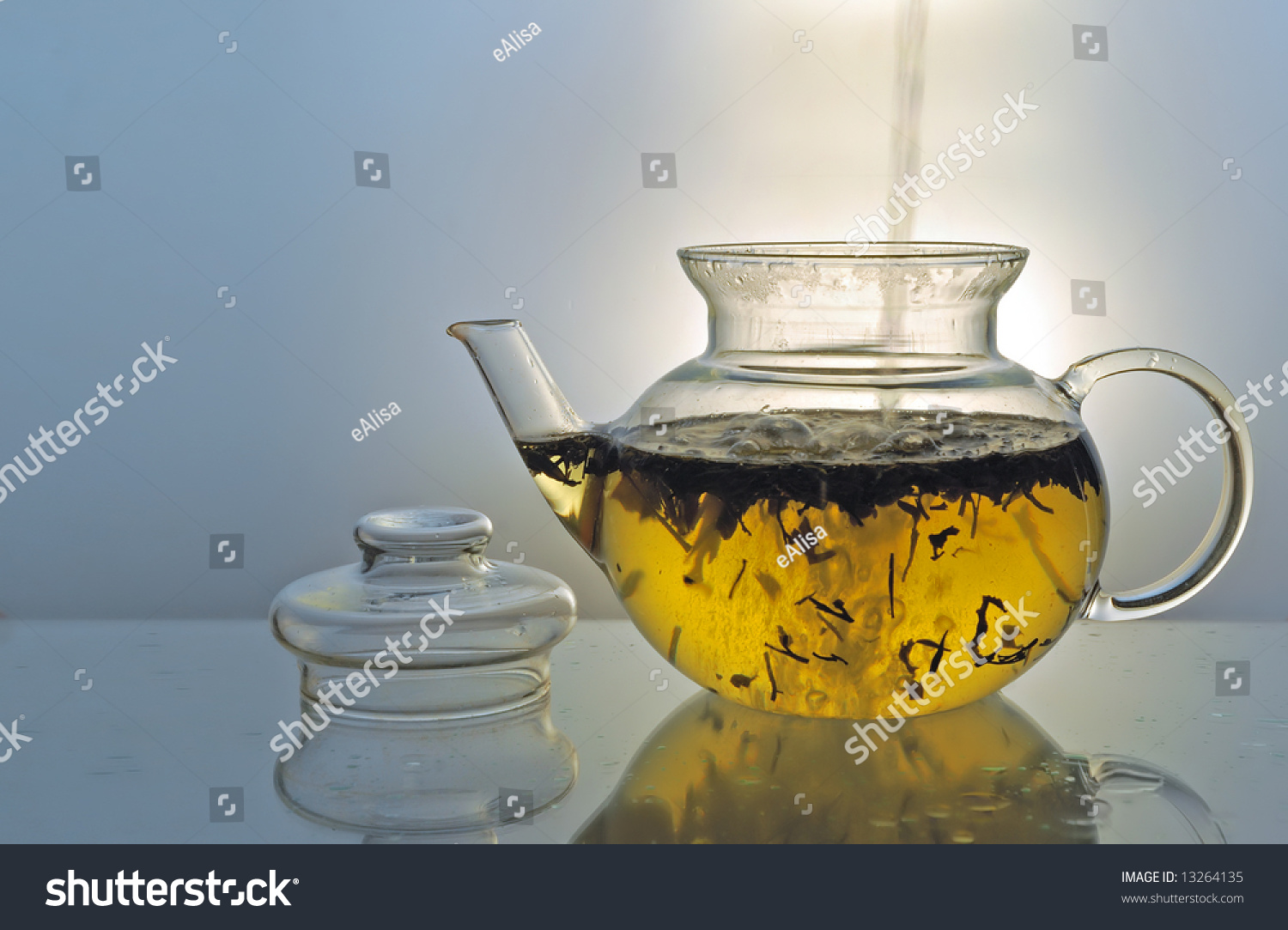 Boil Water Pouring Into Glass Teapot With Green Tea On Blue Background