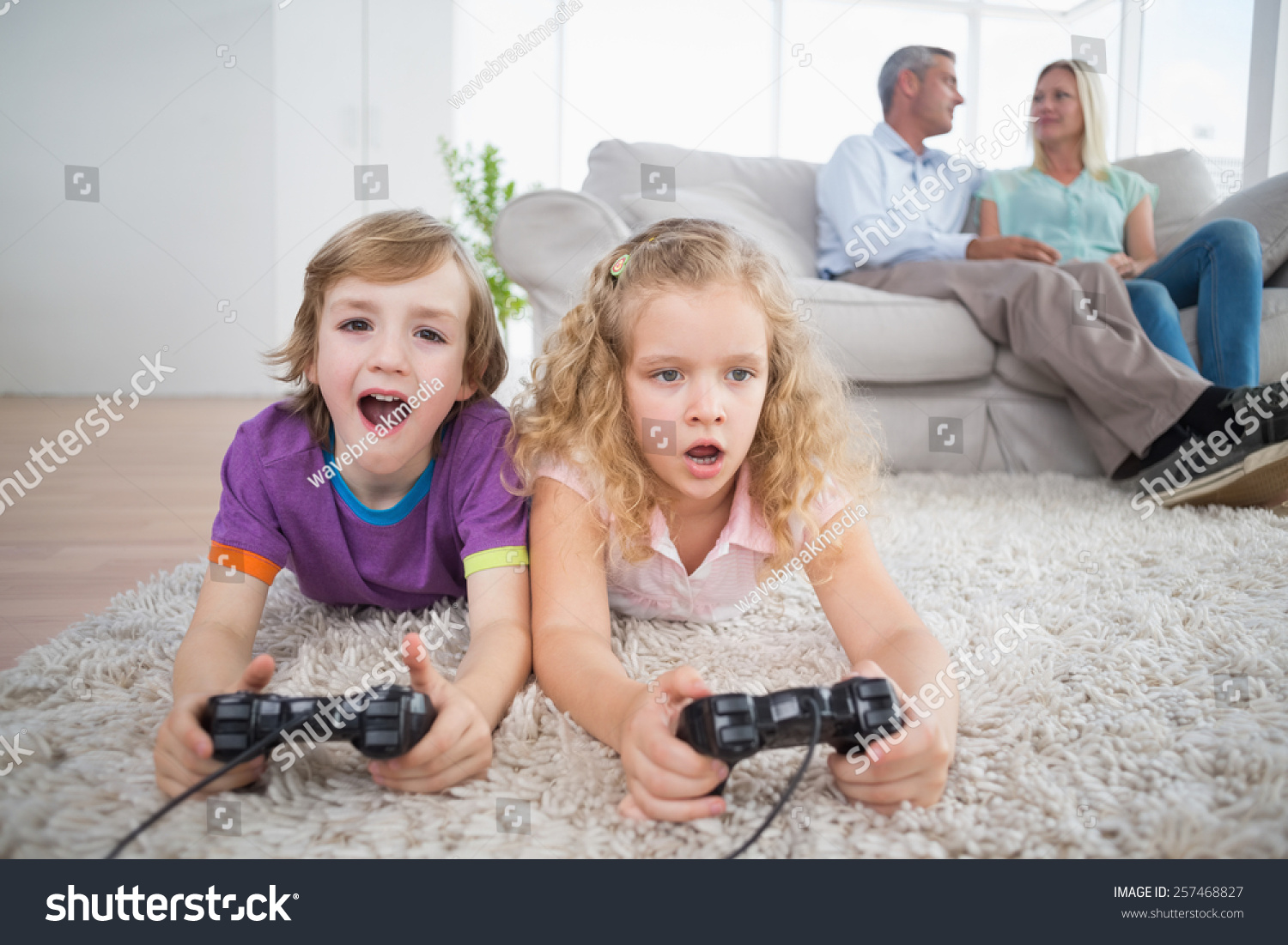 Brother And Sister Playing Video Game While Parents Sitting On