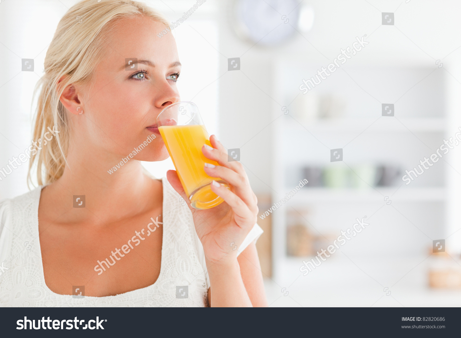 Close Up Of A Blonde Woman Drinking Juice In Her Kitchen Stock Photo