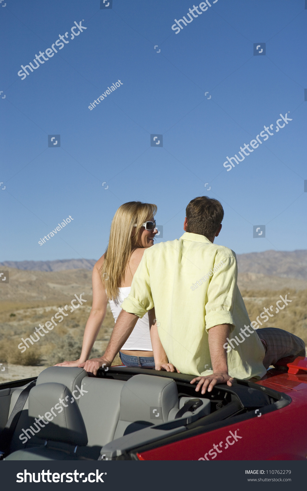 Couple sitting at backside of car looking away Couple sitting at backside of car looking away