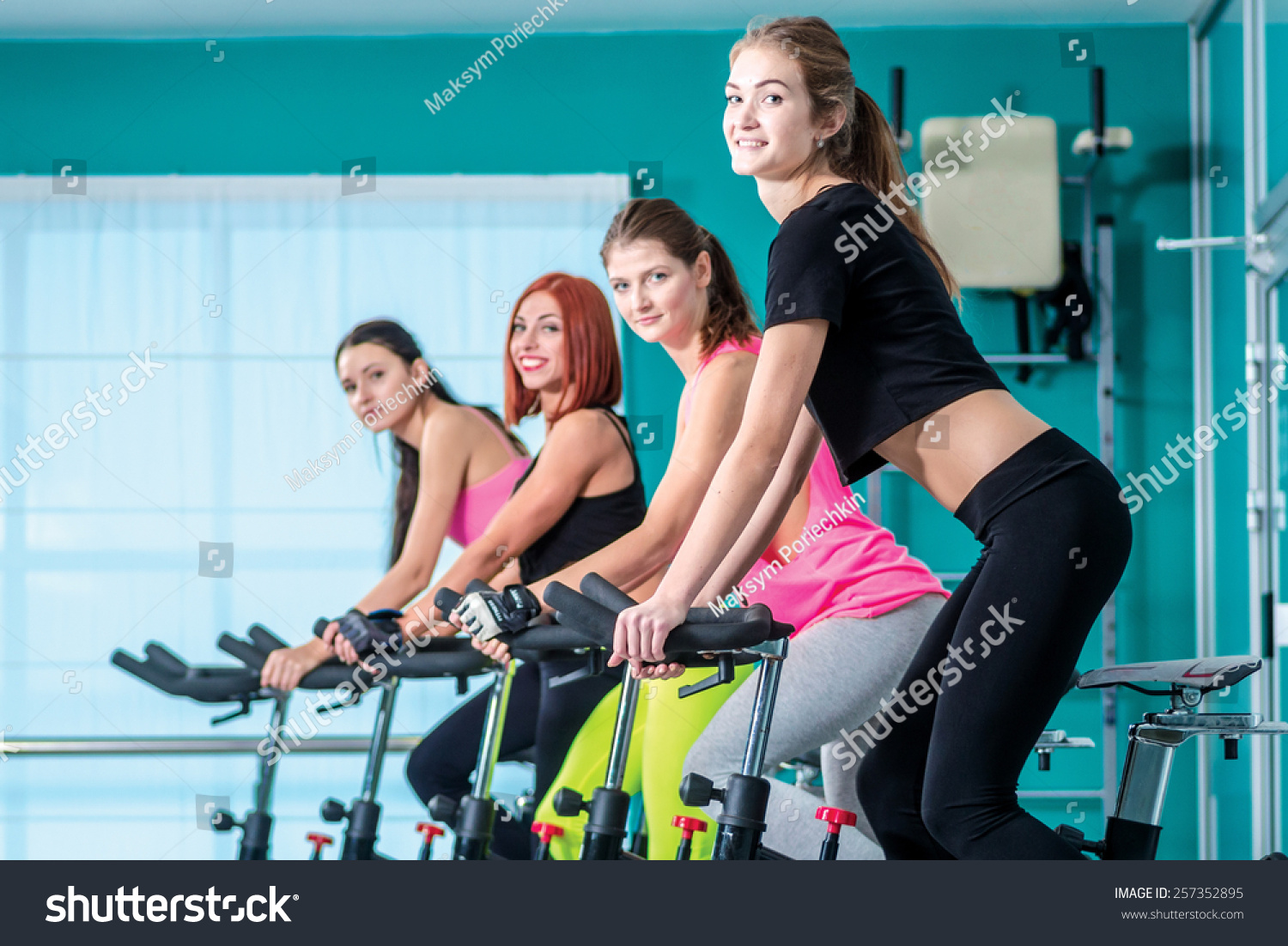 Fitness workout in the gym Athletic girl pedaling on the simulator until her four girlfriends athletes pedaling on a stationary bike at the gym Fitness workout in the gym Athletic girl pedaling on the simulator until her four girlfriends athletes pedaling on a stationary bike at the gym