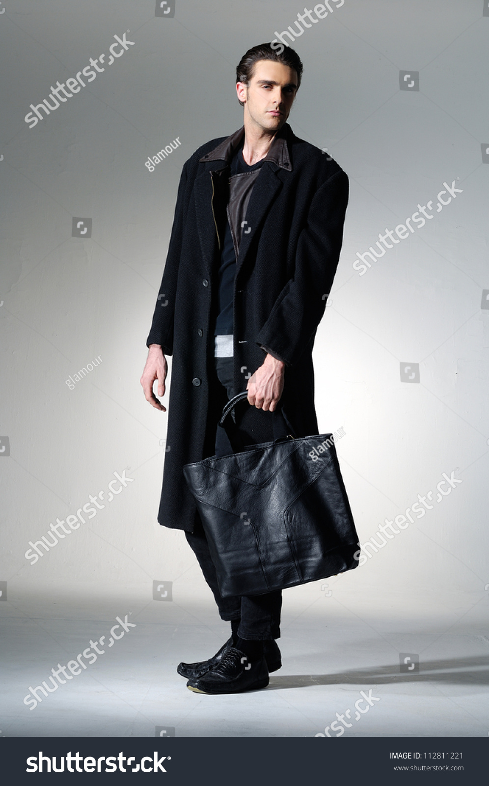 Full Body Fashion Shot Of A Young Man In Coat Holding Black Bag On