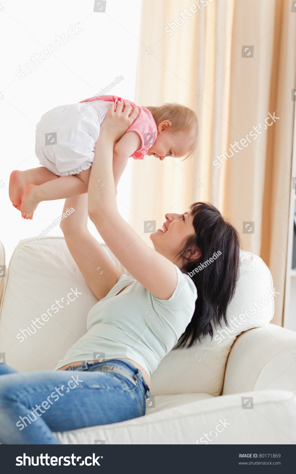 Gorgeous Woman Holding Her Baby In Her Arms While Sitting On A Sofa In