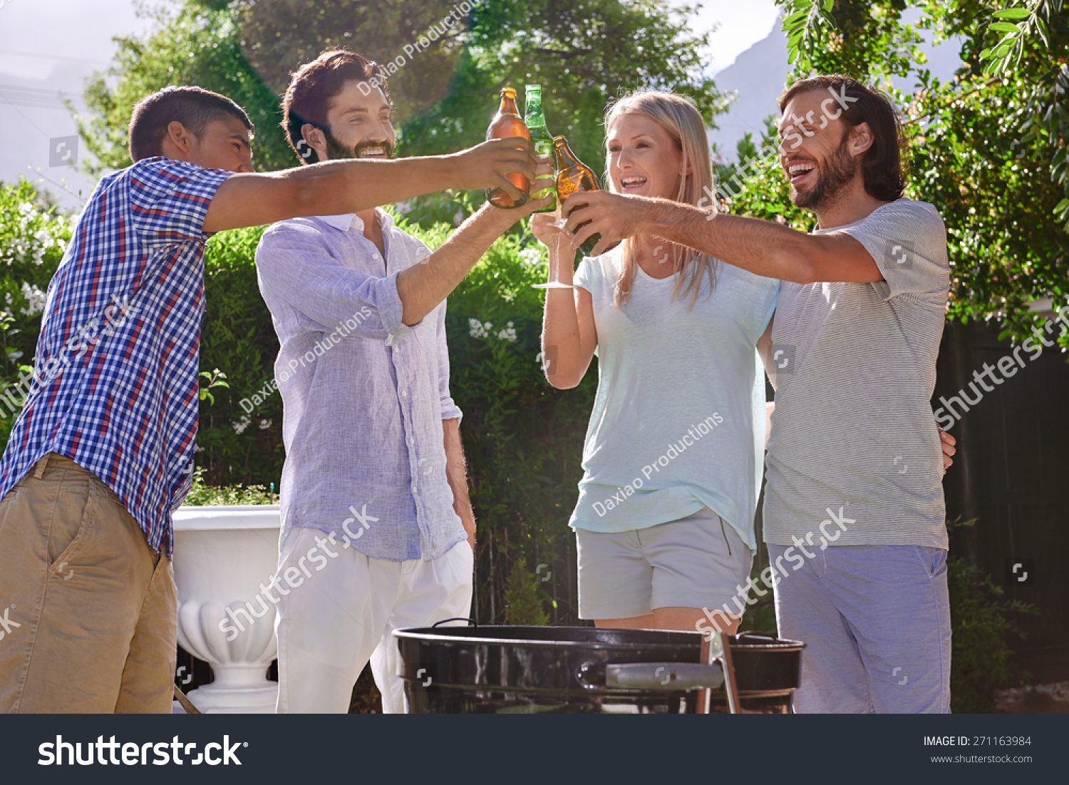 Group Of Friends Having Outdoor Garden Barbecue Laughing Toasting With Alcoholic Beer Drinks