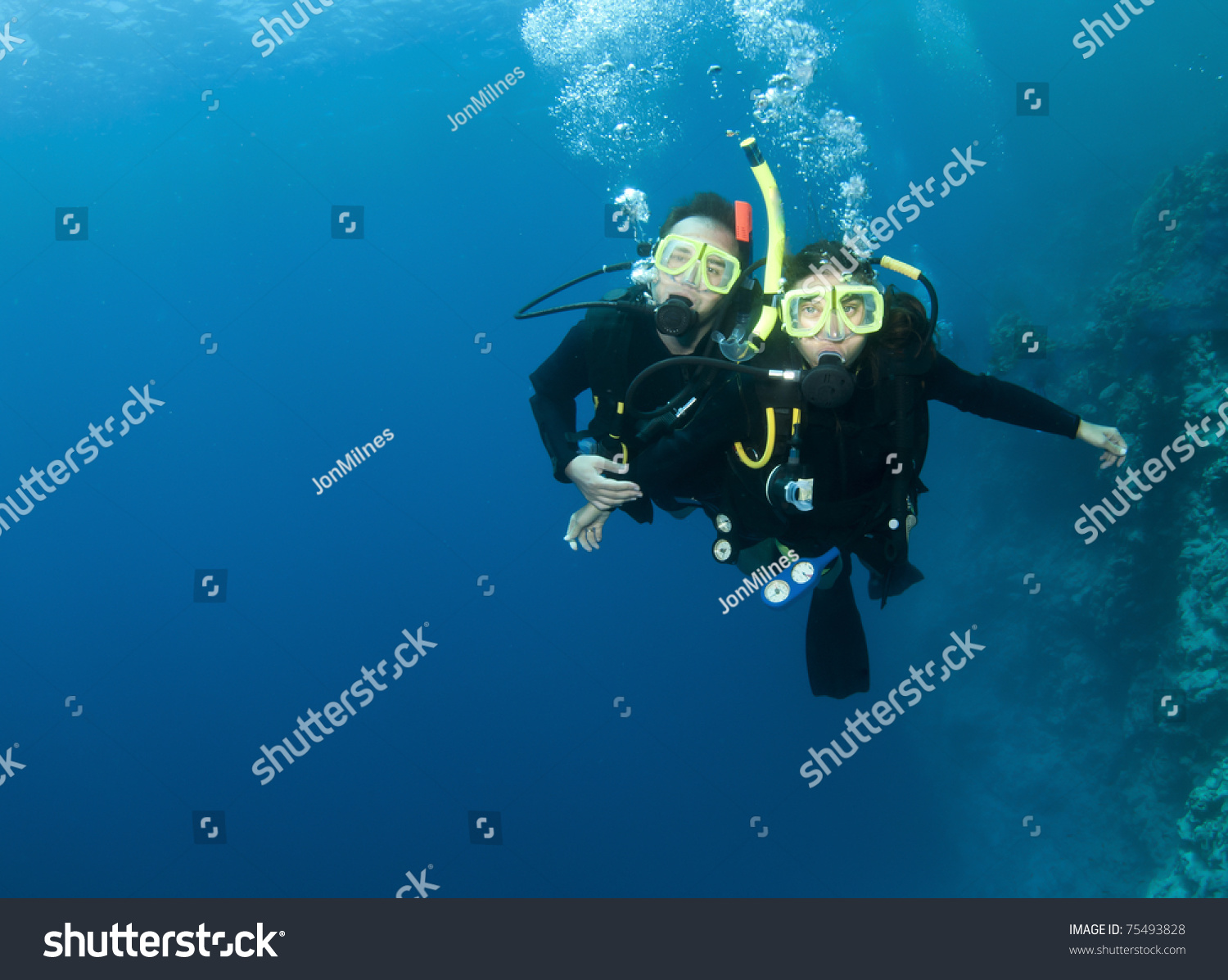Happy Couple Scuba Diving Together In Clear Blue Ocean With Coral Reef