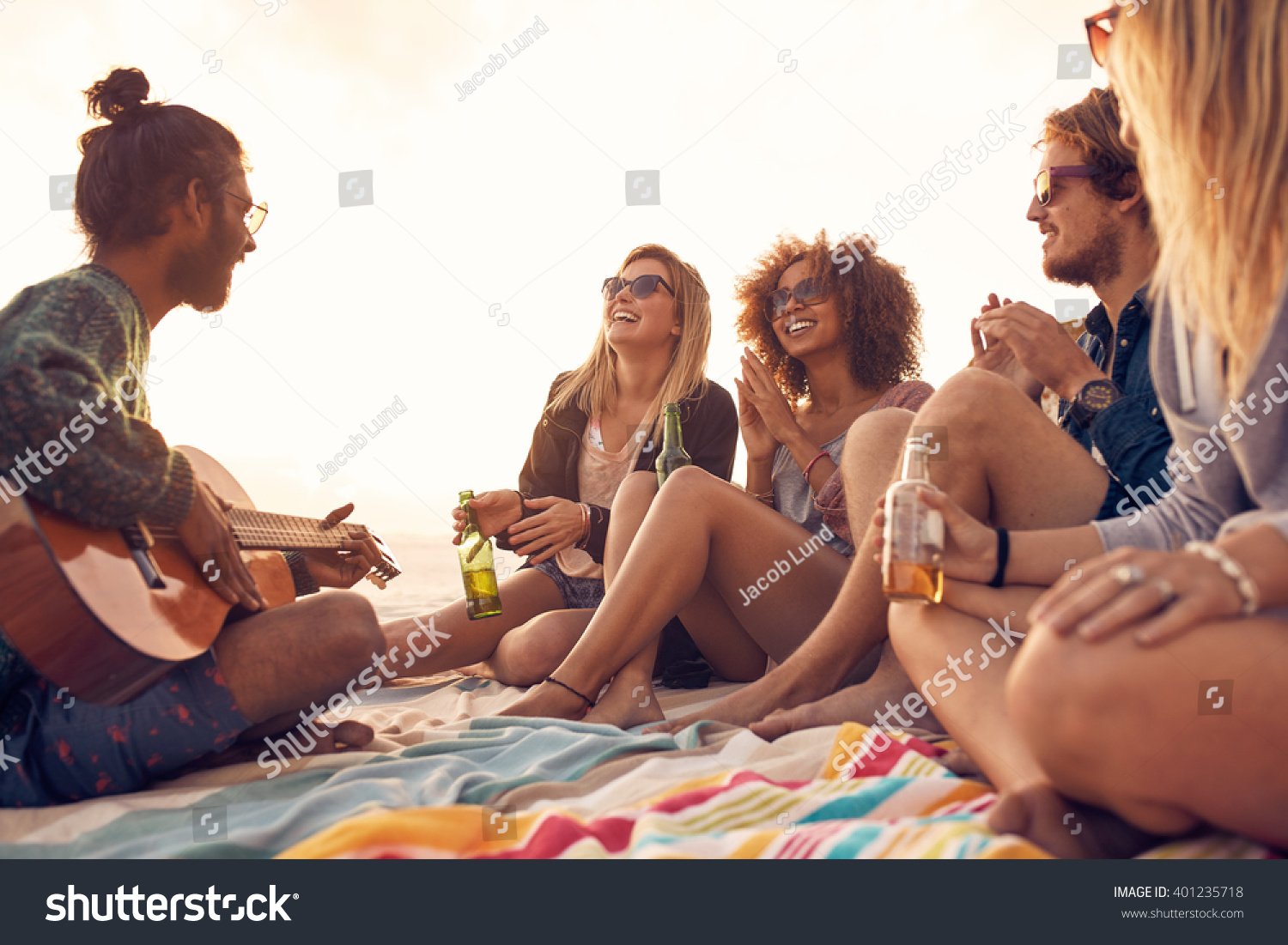 Happy hipsters relaxing and playing guitar at the beach Friends drinking beers and listening to music Having fun at beach party in evening Happy hipsters relaxing and playing guitar at the beach Friends drinking beers and listening to music Having fun at beach party in evening