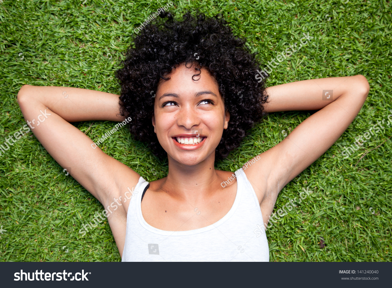 Happy Mixed Race Woman Lying Down On Green Grass With Hands Behind Her