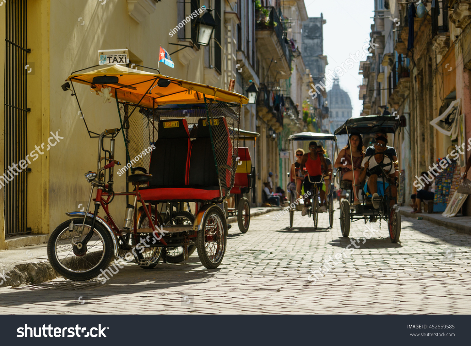 HAVANA CUBA MAY 20 2016 Local taxi in Havana Trishaw without passengers is parked on the street Another taxi is transporting passengers Top of the Capitol is at the end of the street HAVANA CUBA MAY 20 2016 Local taxi in Havana Trishaw without passengers is parked on the street Another taxi is transporting passengers Top of the Capitol is at the end of the street