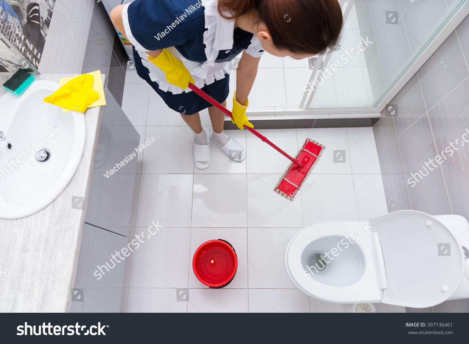 Housekeeper Or Maid In A Neat Uniform And Apron Standing Mopping The
