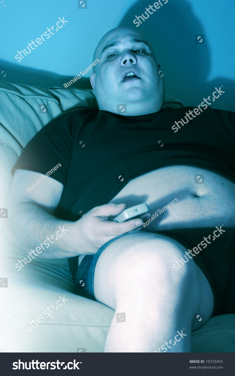 Lazy Overweight Male Sitting On A Couch Watching Television Harsh Blue Lighting From Television