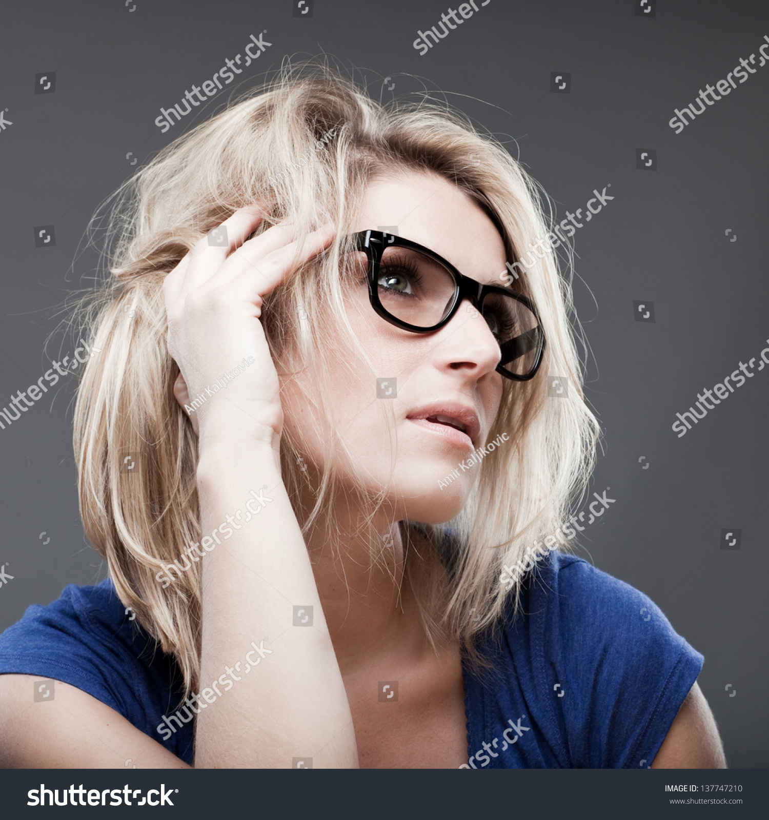 Low Angle Portrait Of A Pensive Blond Woman With Mussed Hair And Heavy Framed Glasses Sitting