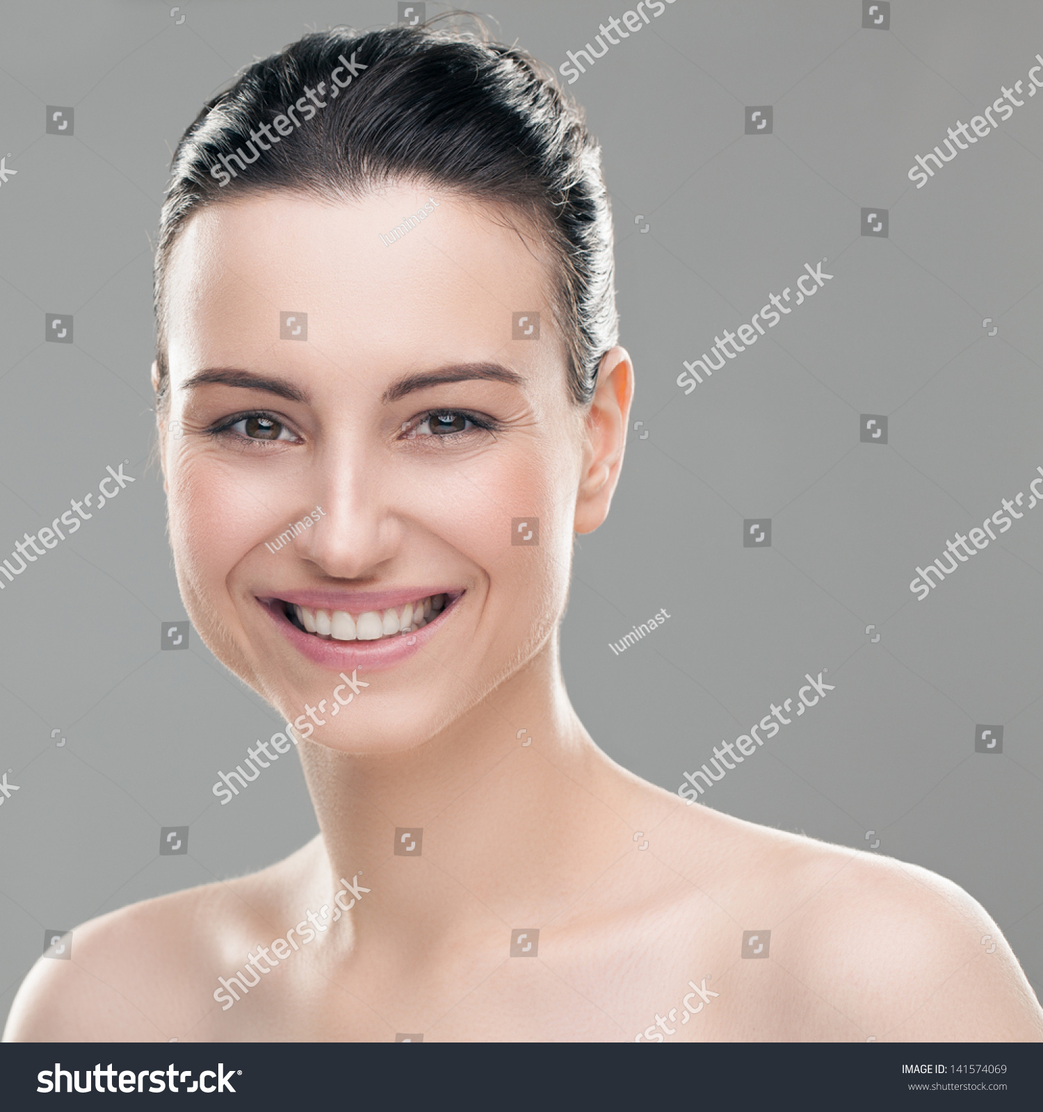 Portrait Of A Smiling Caucasian Woman Posing Topless Against A Gray