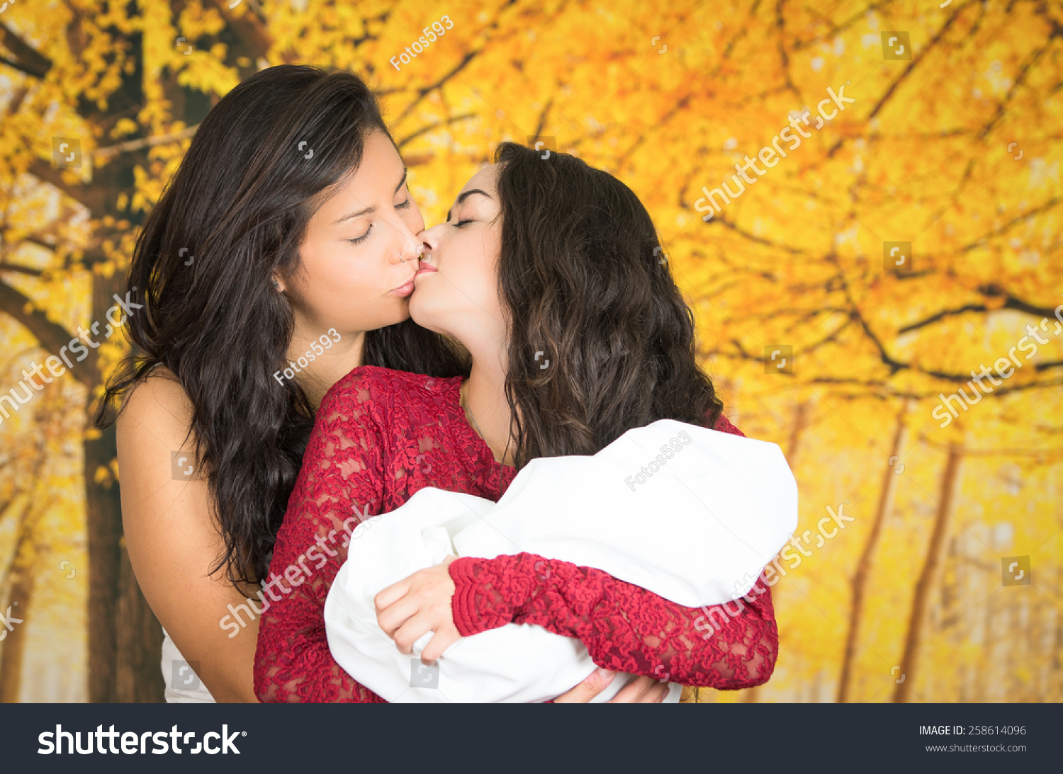 Portrait Of Beautiful Lesbian Couple Holding Their Baby Kissing Over