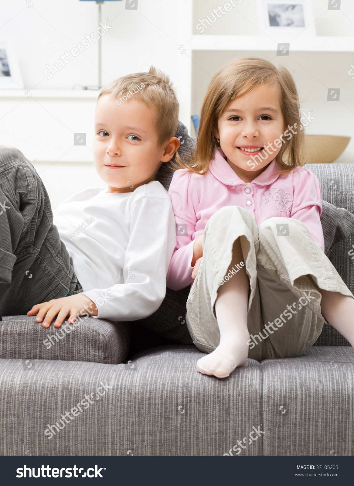 Portrait Of Happy Little Brother And Sister Sitting Together On Couch At Home Smiling Stock