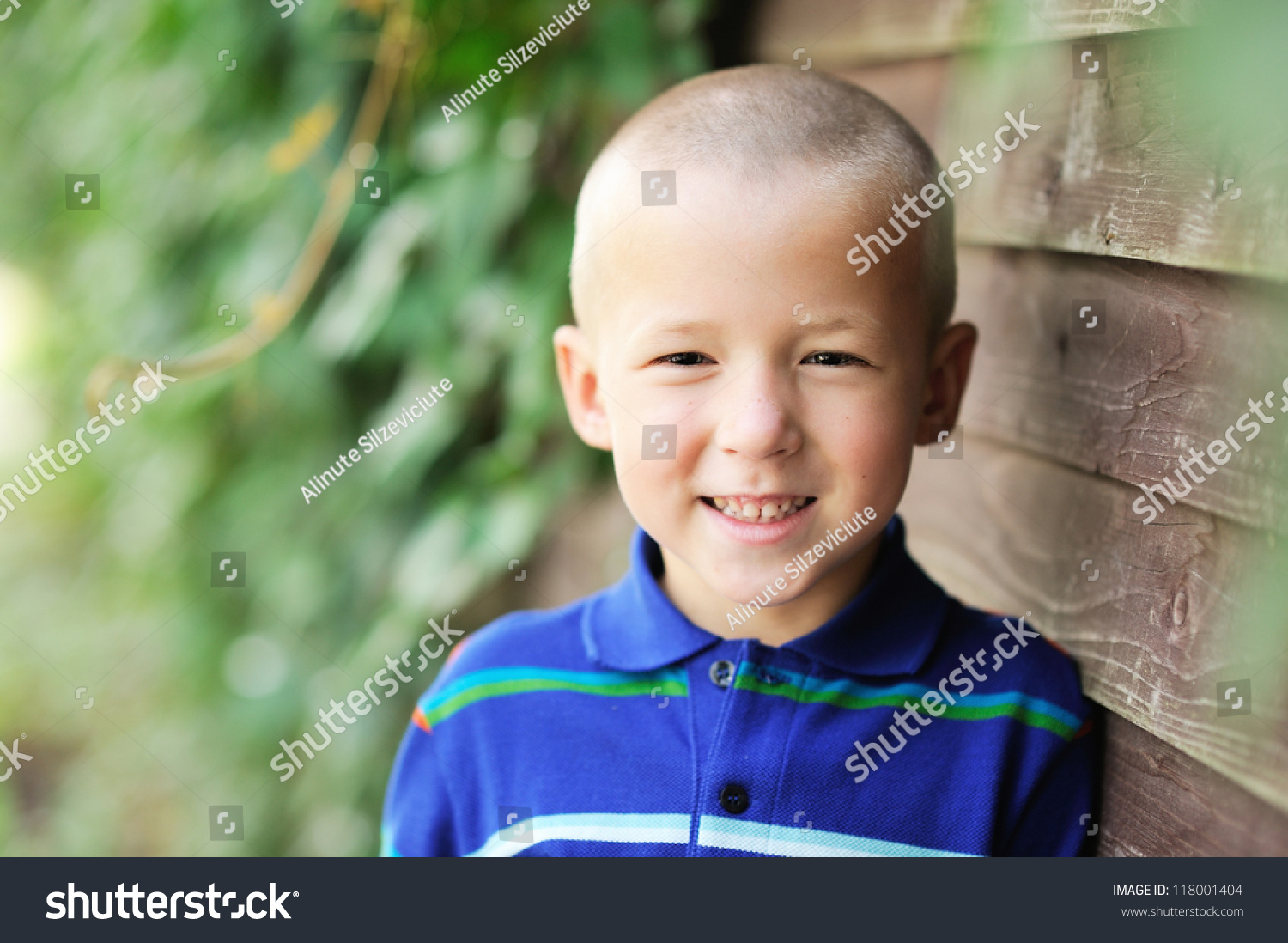 Portrait Of Little Boy Posing Outdoors In Front Of Wooden