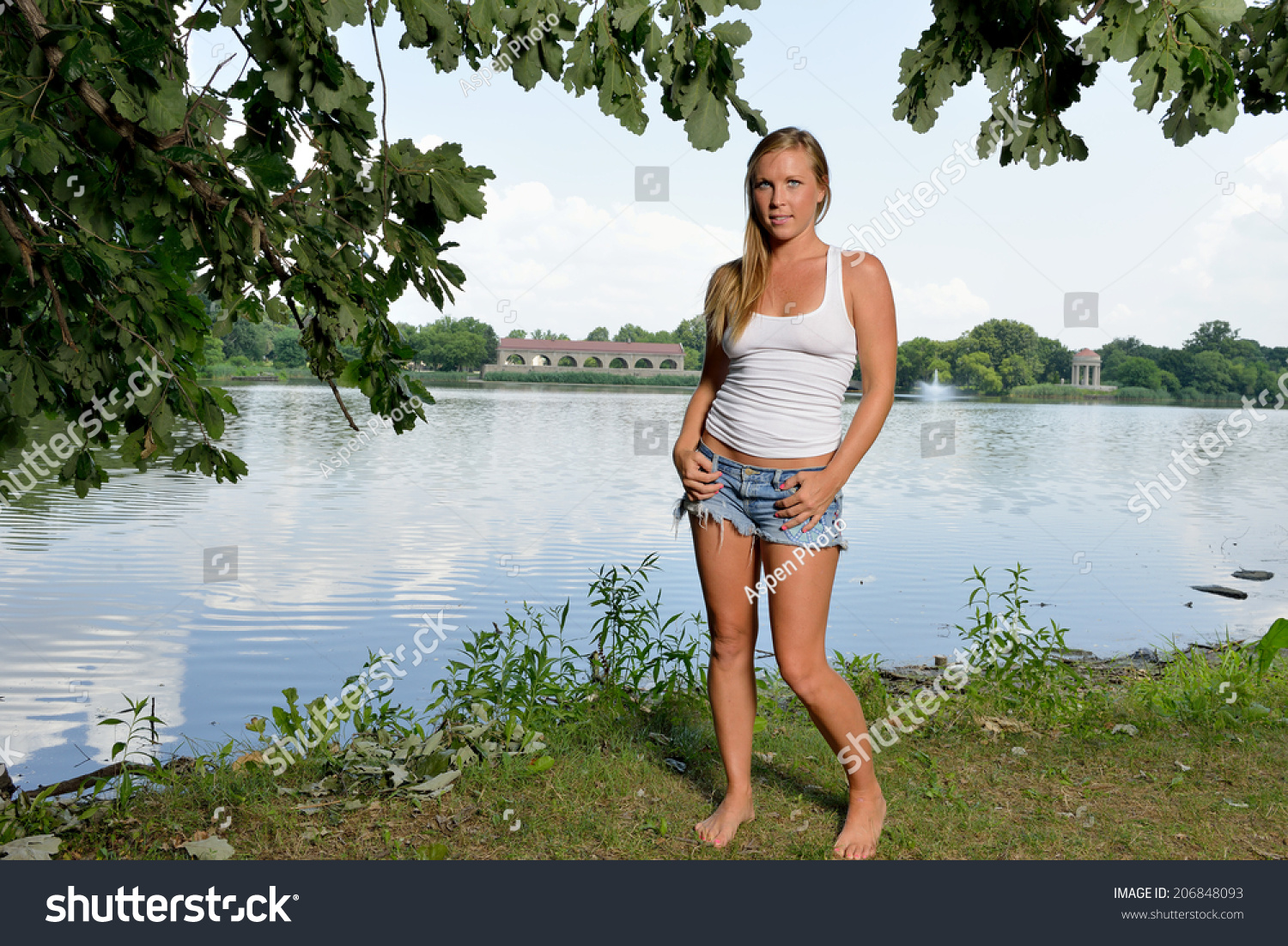 Sexy Blonde Woman In White Tank Top And Denim Cut Off Shorts Standing