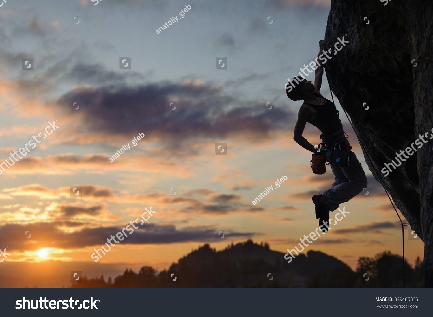 Silhouette of athletic female rock climber climbing steep rock wall against amazing sunset sky in the mountains Girl is hanging on one hand and holding hand in magnesium bag Silhouette of athletic female rock climber climbing steep rock wall against amazing sunset sky in the mountains Girl is hanging on one hand and holding hand in magnesium bag