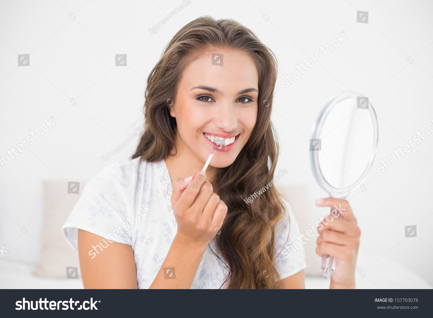 Smiling Attractive Brunette Applying Lip Gloss And Holding Mirror In