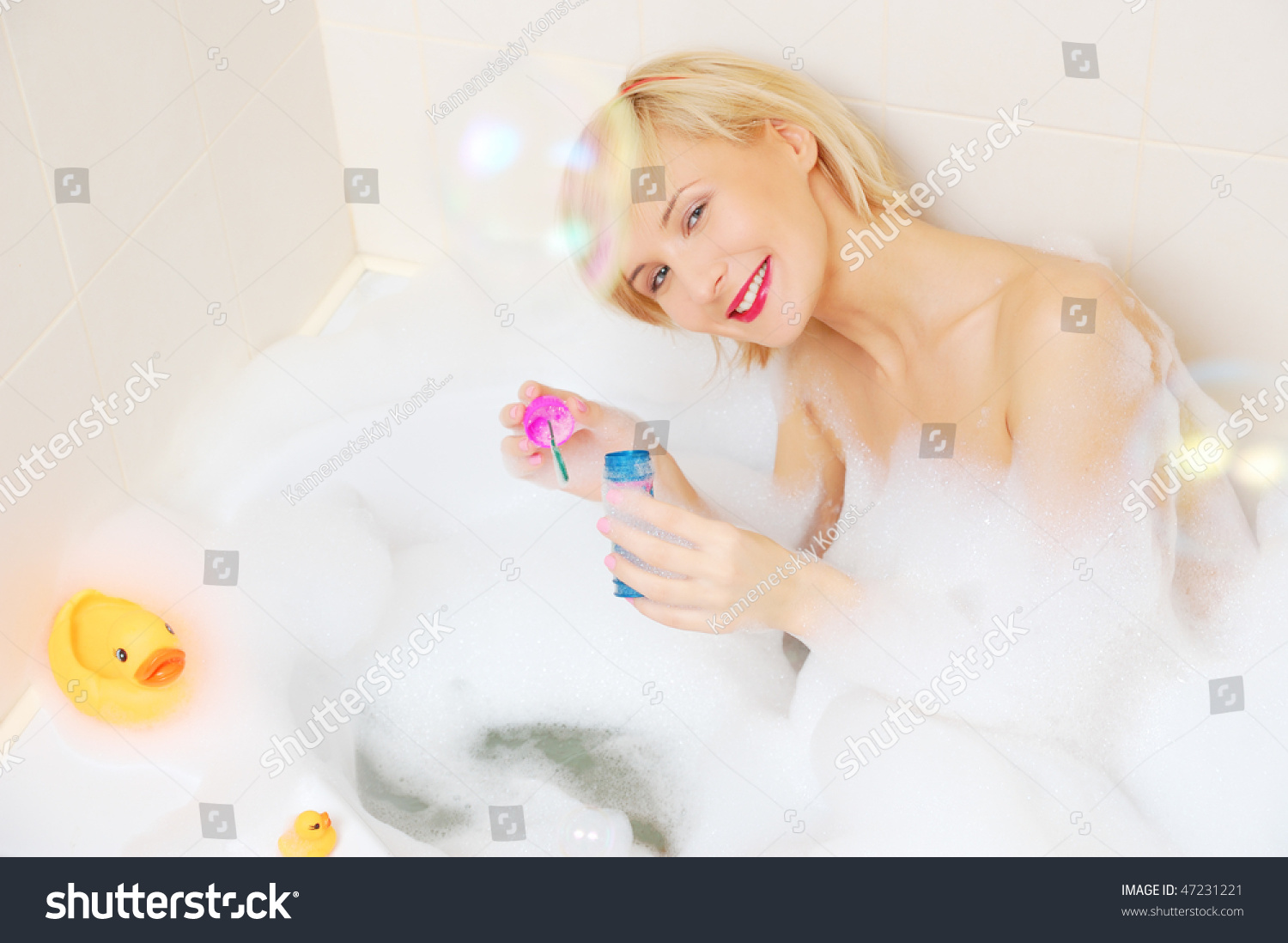Smiling Blond Woman Lying In Bubble Bath With Toy Duck Stoc