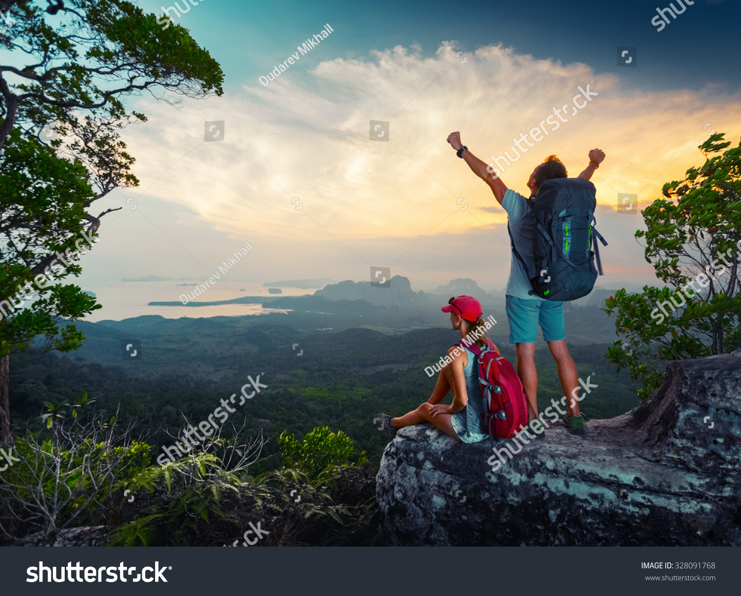 Two hikers relaxing on top of the mountain and enjoying sunset valley view Two hikers relaxing on top of the mountain and enjoying sunset valley view