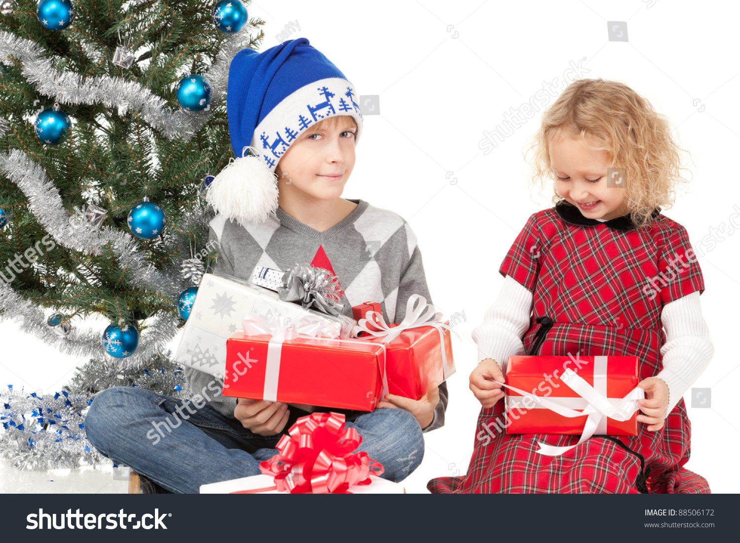 Two Kids Unwrapping Their Christmas Presents Sitting On The Floor Near The New Year Tree, Over