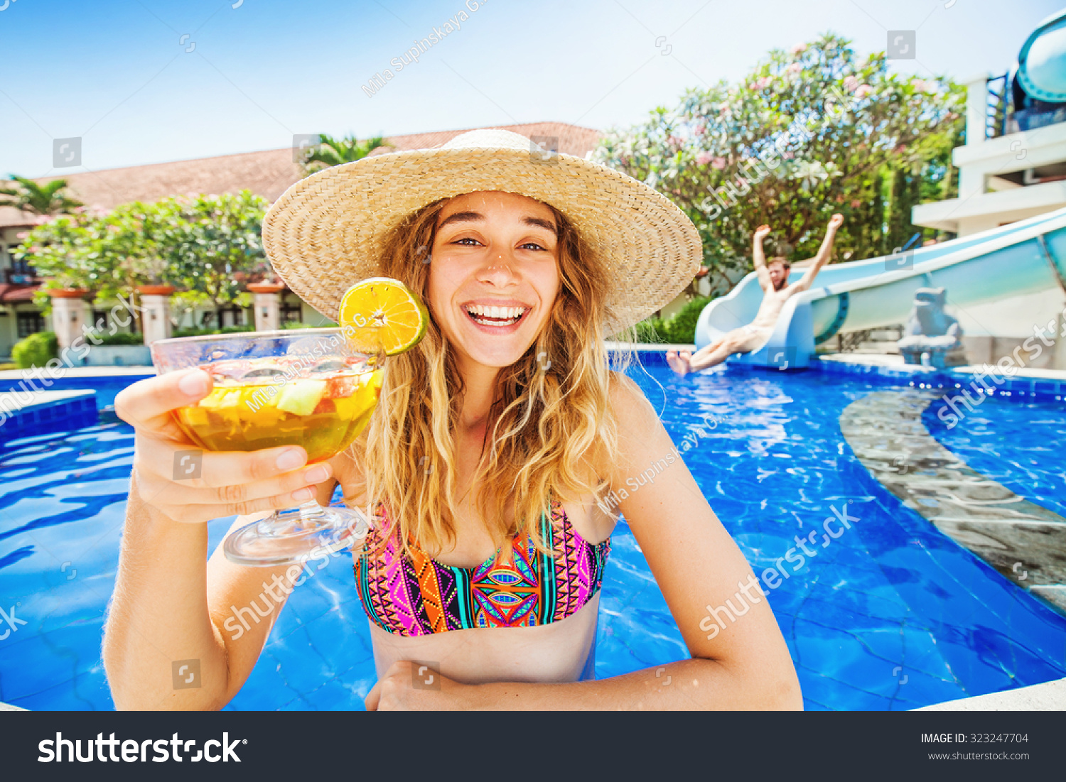 woman in a swimming pool of waterpark holding cocktail and man sliding from the water slide woman in a swimming pool of waterpark holding cocktail and man sliding from the water slide