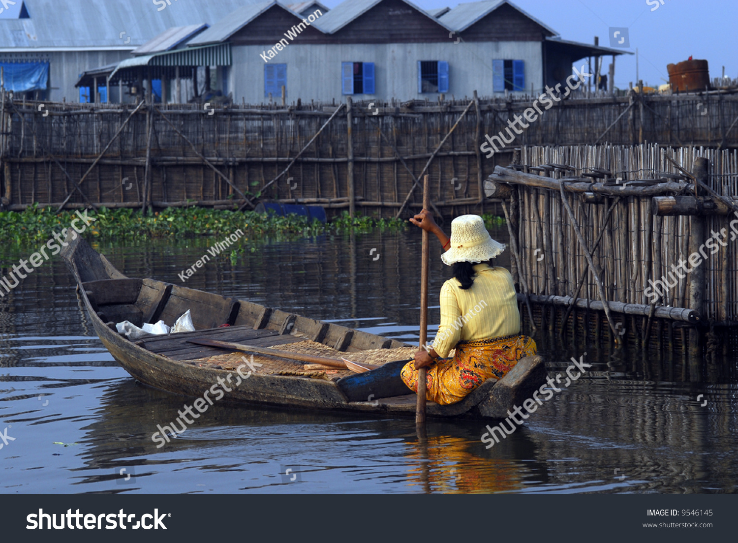 Woman Paddling A Dugout Canoe Through A Floating Village In Siem Reap