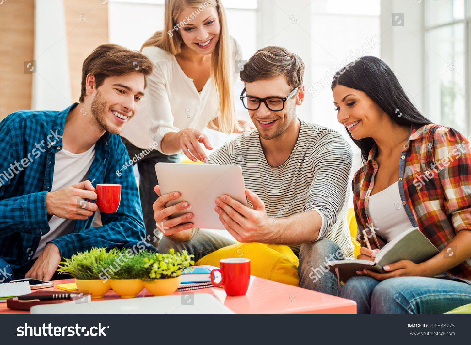 Working on creative project together Group of happy young people looking at digital tablet while sitting on the colorful bean bags in office Working on creative project together Group of happy young people looking at digital tablet while sitting on the colorful bean bags in office