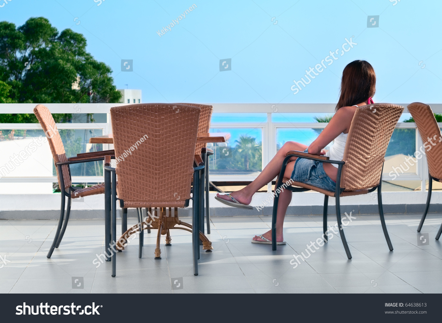 Young beautiful girl sitting on a chair on the balcony of the hotel and looks into the distance. one caucasian woman is back sid.