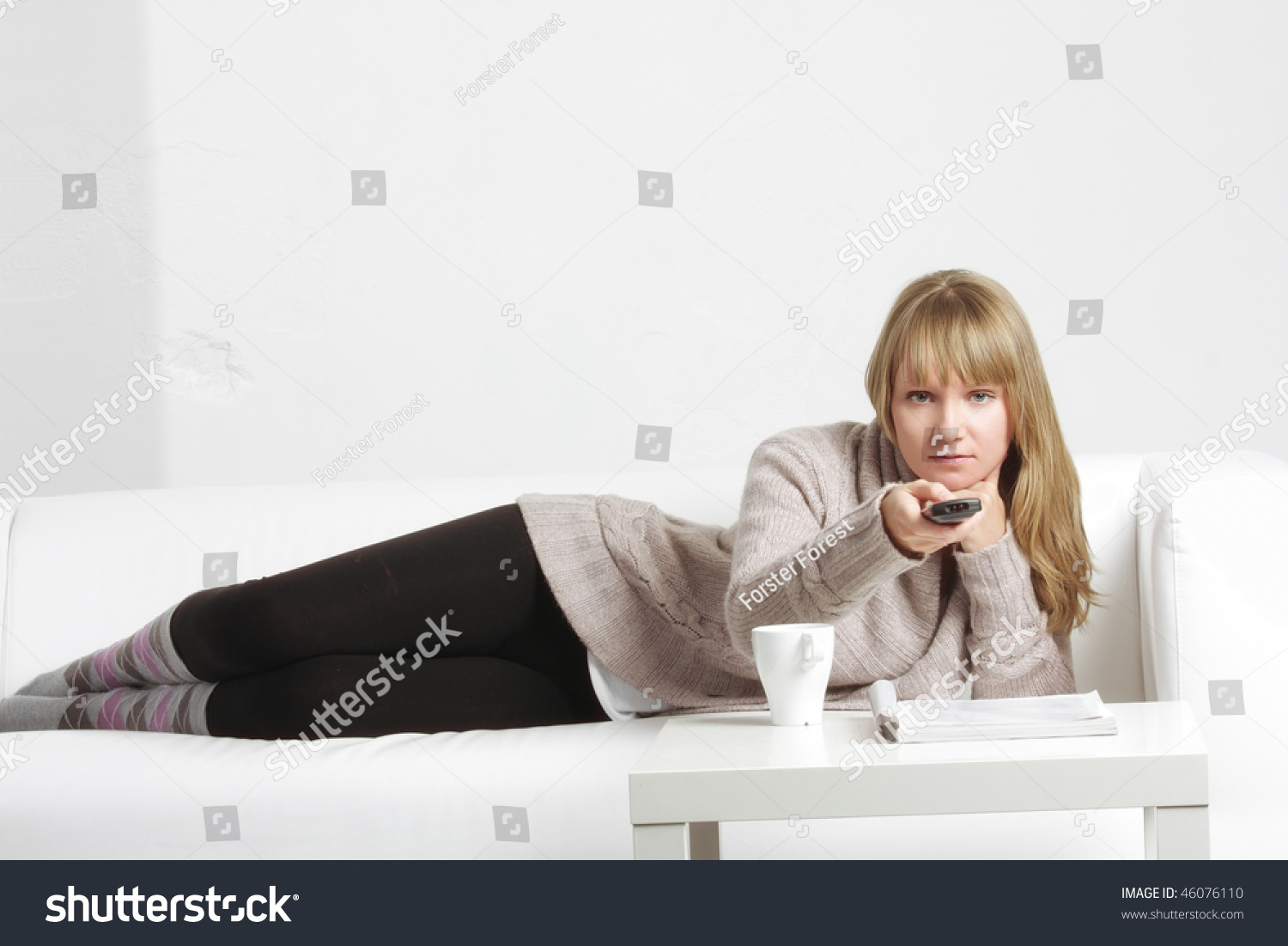 Young Blonde Woman Laying Down On Sofa With Remote Control Sto