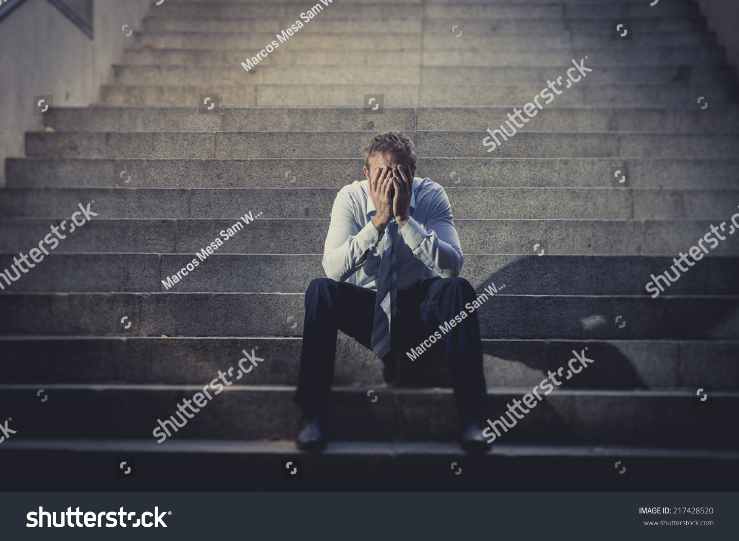 Young business man crying abandoned lost in depression sitting on ground street concrete stairs suffering emotional pain sadness looking sick in grunge lighting Young business man crying abandoned lost in depression sitting on ground street concrete stairs suffering emotional pain sadness looking sick in grunge lighting
