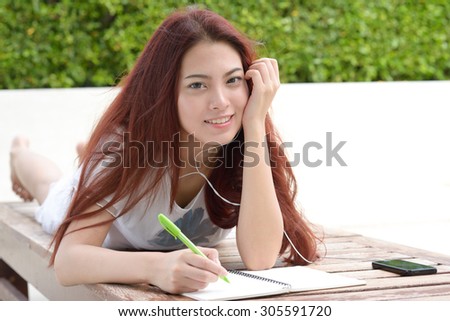 Woman lying in a bench with listening to the music from a smart phone and writing note.